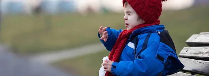 Un copil strănută pe o bancă în parc iarna