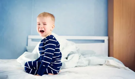 Un copil mic plângând pe un pat nefăcut
