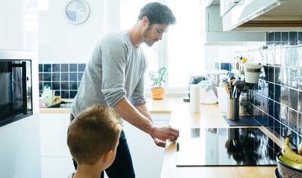 Muškarac čisti radnu površinu u kuhinji dok ga dijete pažljivo promatra
