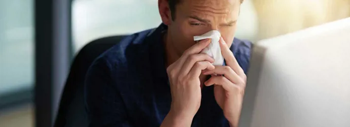 Kýchající muž hledá na počítači inkubační dobu svého nachlazení