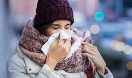 Žena zamotana u glomaznu zimsku odjeću boluje od simptoma sinusitisa i kiše u maramicu na otvorenom
