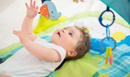 Dítě ležící na barevné podložce a hrající si s hračkami, které mu visí nad hlavou