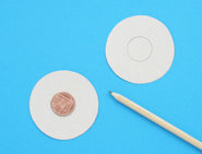 Zwei ausgeschnittene Kreise aus Pappe auf einer blauen Fläche mit einer Münze in der Mitte und einem Bleistift an der Seite.