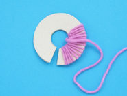 Ein dicker, ringförmiger Pappausschnitt der mit lila Wolle umwickelt wird.