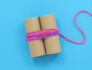 Zwei Toilettenpapierrollen, die in der Mitte mit rosa und violetter Wolle zusammengewickelt sind als erster Schritt Pompons-Selbermachen-Anleitung.