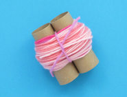 Weitere Lagen rosa Wolle werden um die Rollen gewickelt und bilden eine 3 cm dicke Schlaufe, die mit einer rosa Wollschnur befestigt wird.