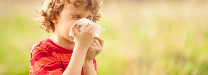 Ένα αγόρι με αλλεργία στη γύρη φυσάει τη μύτη έξω του σε ένα χωράφι