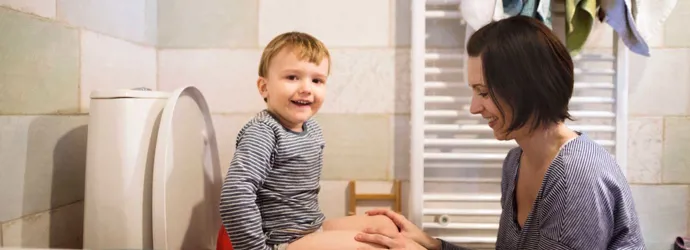Μια μητέρα βοηθά τον γιο της να καθίσει στη λεκάνη της τουαλέτας