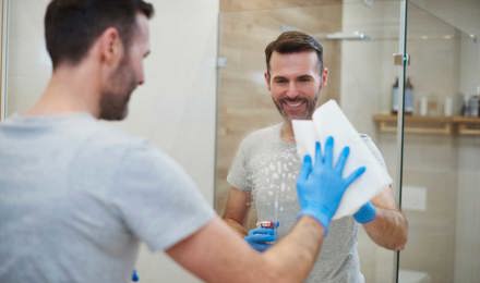 Eine Frau, die blaue Putzhandschuhe trägt, putzt einen Spiegel im Badezimmer
