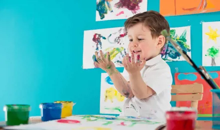 Ein Kind sitzt an einem Tisch und malt mit den Fingern