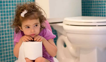 Маленькая девочка сидит на горшке и держит рулон туалетной бумаги в руках
