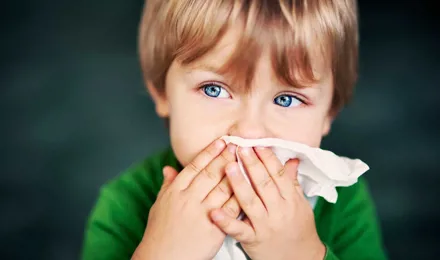 Мальчик с аллергией на пыль держит бумажную салфетку перед его носом