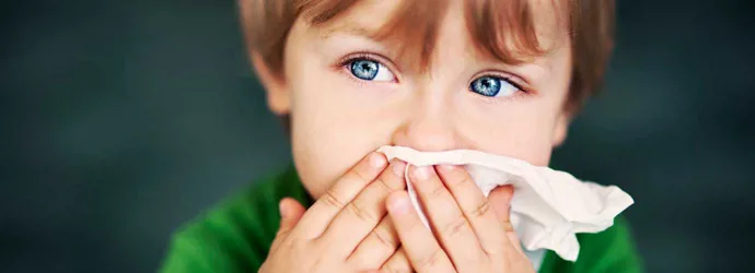 Мальчик с аллергией на пыль держит бумажную салфетку перед его носом