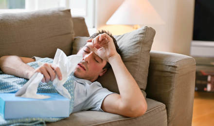 Человек лежит на диване с гриппом, держа салфетки