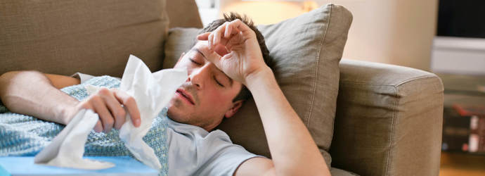 Человек лежит на диване с гриппом, держа салфетки