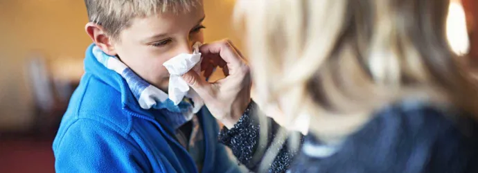 Мать сморкает нос своего ребенка, которому может быть интересно, что нужно сделать, чтобы предотвратить простуду от дальнейшего распространения