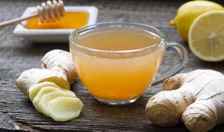 Целый и нарезанный имбирь, мед, лимон, и стакан смеси на деревянном столе