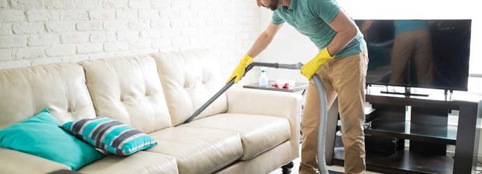 Человек чистит белую ткань дивана с пылесосом