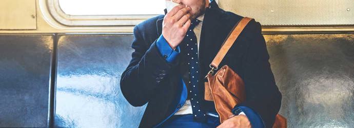 Egy öltönyös férfi ül a vonaton az orrát fújva