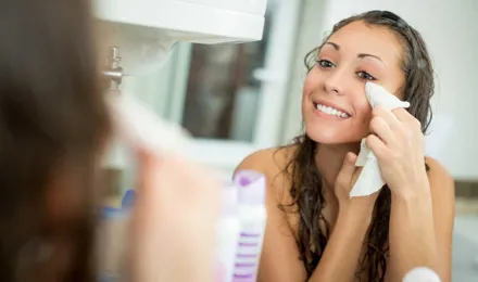 Žena se smiješi dok uklanjanja šminku s lica vlažnom maramicom