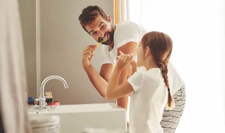 Muž a jeho mladá dcera se učí šetřit vodou při čistění zubů v koupelně