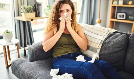 Femeie cu simptome de alergie sau răceală își suflă nasul