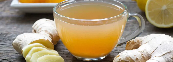 Ghimbir întreg și tocat, miere, lămâie și un pahar cu acestea amestecate, toate pe o masă de lemn