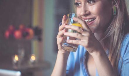 Женщина держит стакан воды с нарезанным лимоном в нем 