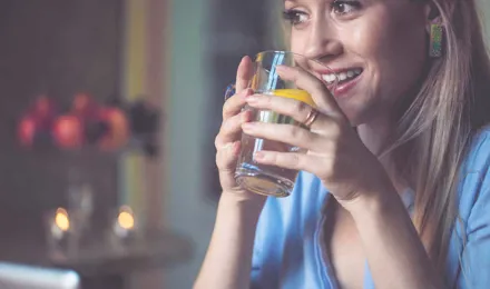Женщина держит стакан воды с нарезанным лимоном в нем 