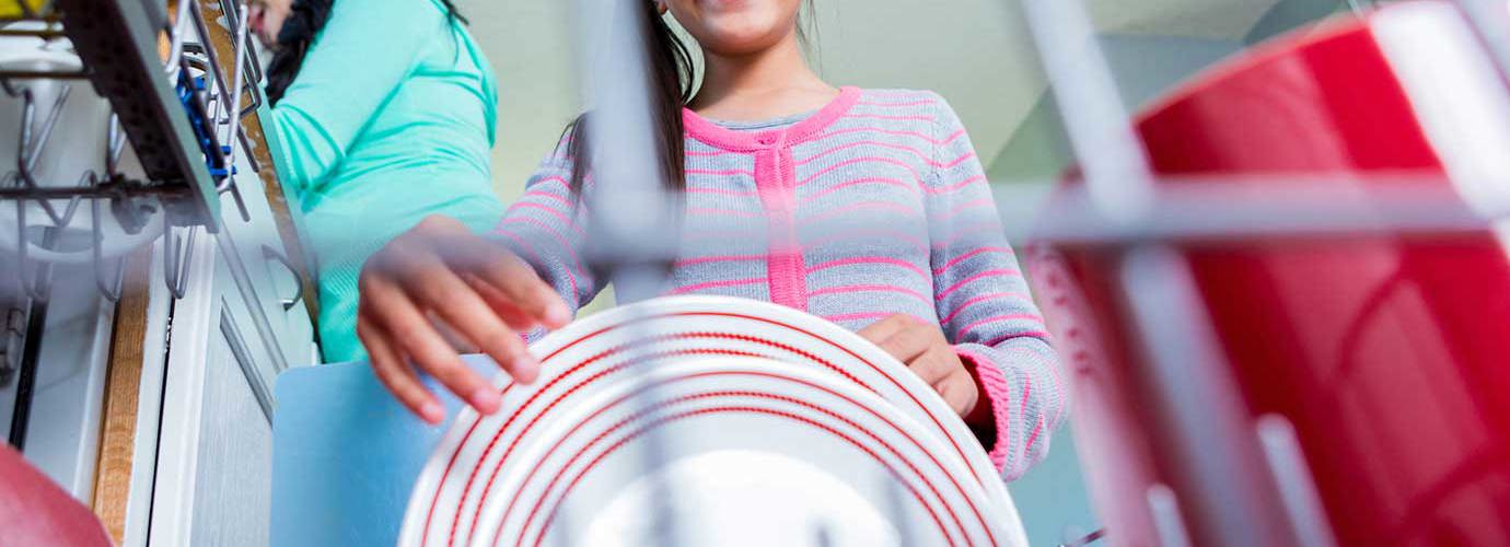 Девочка помогает ее матери на кухне загружая или разгружая посудомоечную машину