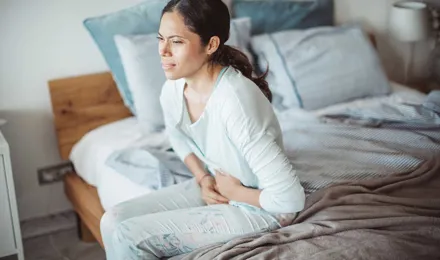 Eine Frau sitzt mit Schmerzen im Unterleib auf einem Bett