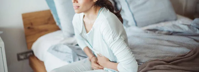 Жена седи на леглото си с болки в корема
