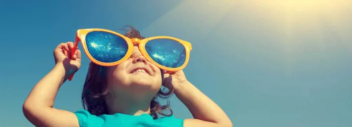 O tânără copilă, purtând în mod hilar o pereche prea mare de ochelari de soare, într-o zi senină, luându-și doza de vitamina D de la soare