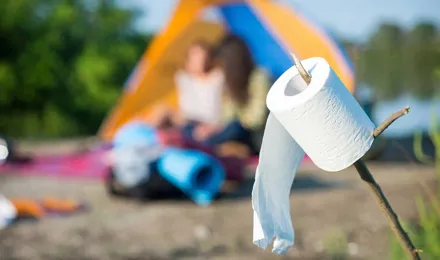 Eine Rolle Toilettenpapier auf einem Stock aufgespießt mit einem Campingplatz im Hintergrund