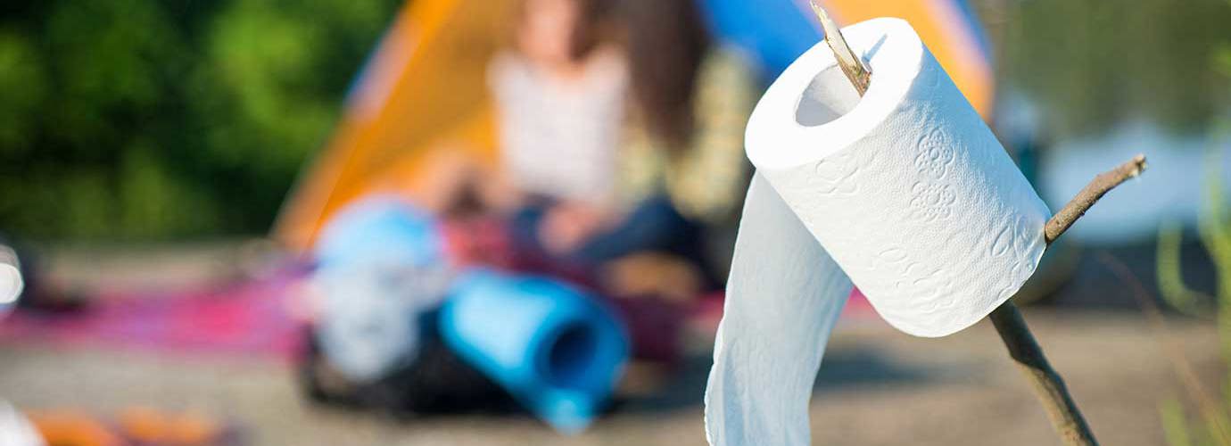 Eine Rolle Toilettenpapier auf einem Stock aufgespießt mit einem Campingplatz im Hintergrund